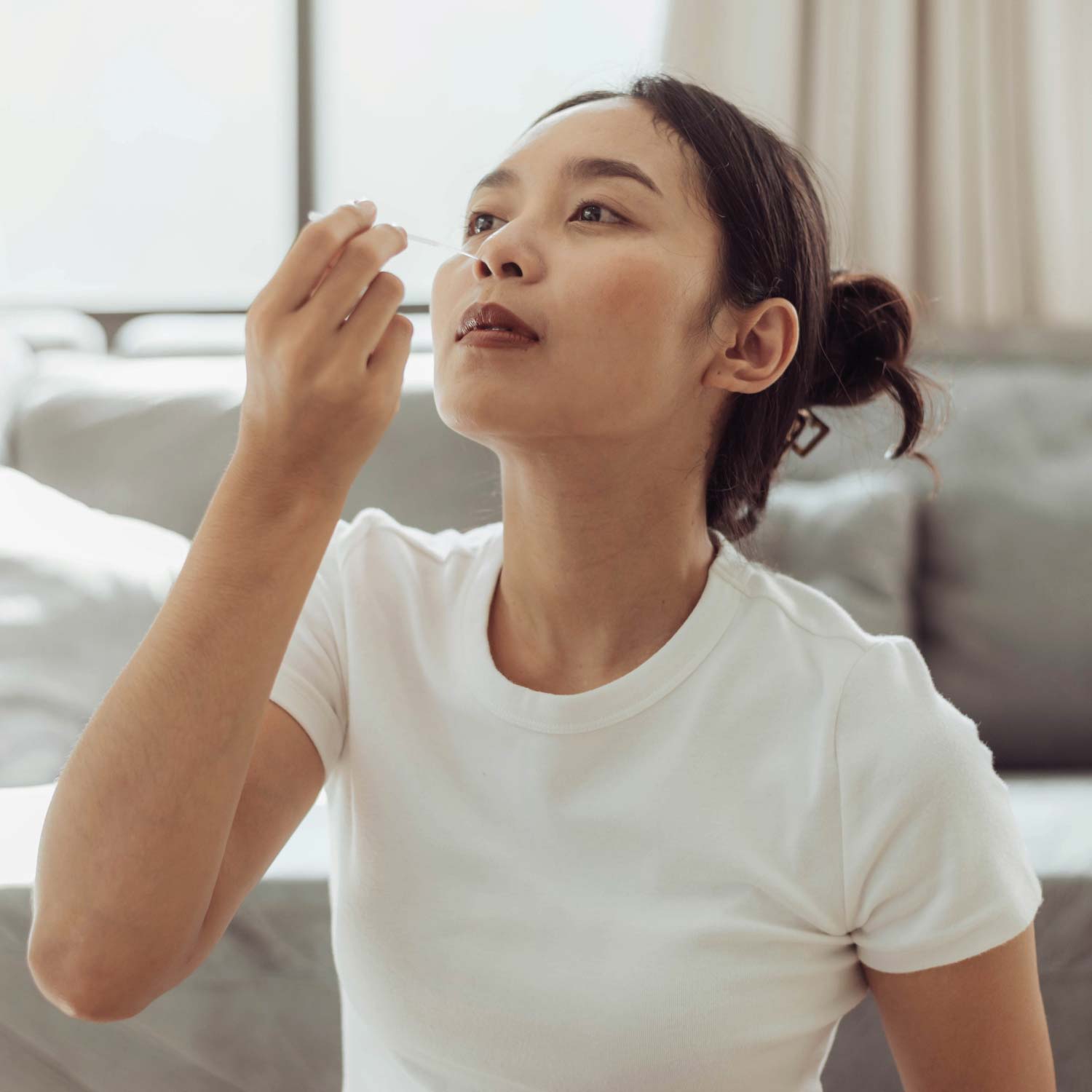 Asian woman performing nasal swab using Atron COVID-19 Rapid Antigen Test Home Kit