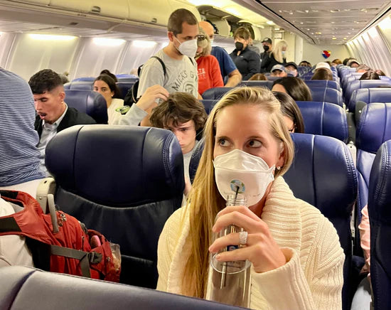 Woman drinking water on airplane in Canada using SIP mask valve with straw